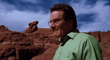 a man wearing glasses and a green shirt is standing in front of a rock formation