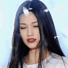 a close up of a woman 's face with her eyes closed and feathers falling from her hair .