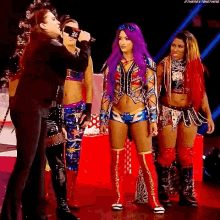 a group of women are standing next to each other on a stage and one of them is wearing purple hair .