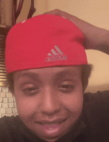 a young man wearing a red adidas hat