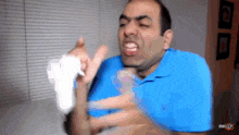 a man in a blue shirt is making a funny face while holding a white object