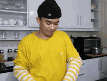a man wearing a yellow shirt and striped sleeves is cooking in a kitchen