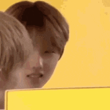 a man is looking at another man 's face while sitting in front of a yellow wall .