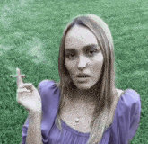 a woman in a purple shirt is smoking a cigarette .