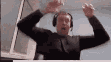 a man wearing headphones is standing in front of a window with his hands in the air .
