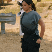 a woman in a blue shirt and black pants is walking in the dirt