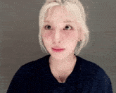 a woman with blonde hair and red cheeks is wearing a blue t-shirt and earrings .