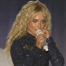 a blonde woman singing into a microphone in a blue shirt