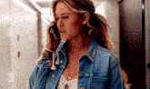 a woman wearing a denim jacket is talking on her cell phone .