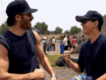two men wearing hats and sunglasses are standing next to each other and talking .