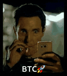 a man smoking a cigarette while looking at his phone with the word btc on the bottom right