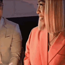 a woman in a pink jacket is smiling while standing next to a man in a tan suit