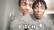 a man with dreadlocks is wearing a necklace and the word bitch is on the front of his shirt .