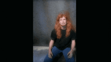 a man with long red hair is sitting in front of a concrete wall