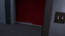 a man is standing in a dark room behind a red door .