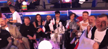 a group of people sitting in a stadium with a man wearing a guess shirt