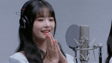 a girl wearing headphones stands in front of a microphone with her hands folded