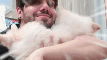 a man with a beard is holding a small white puppy in his arms .