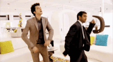 two men in suits are dancing in a living room in front of a couch .