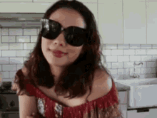 a woman wearing sunglasses and an off the shoulder top is standing in a kitchen