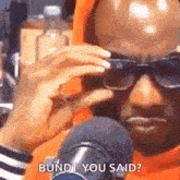 a man wearing sunglasses is talking into a microphone while holding his hand to his face .