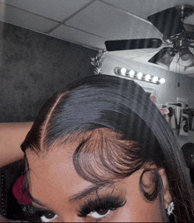 a close up of a woman 's hair with a ceiling fan behind her
