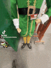 a mannequin dressed in a green elf costume has a name tag that says mari.harvests money
