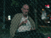 a man smoking a cigarette behind a chain link fence at night