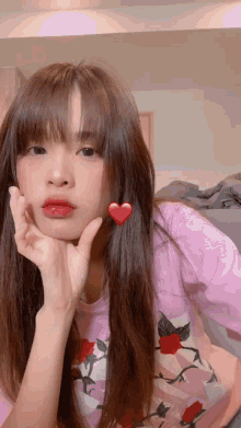 a woman wearing a pink shirt with roses on it has a red heart on her ear