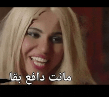 a woman with blonde hair is smiling with arabic writing on the bottom of her face .