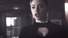 a woman in a black dress and earrings is standing in a dark room looking at the camera .