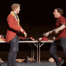 a man in a red jacket stands next to a man in a plaid shirt