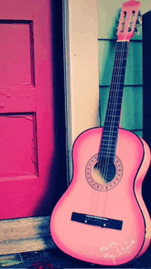 a pink guitar is leaning against a pink door that says music my life