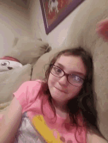 a girl wearing glasses and a pink shirt laying on a bed