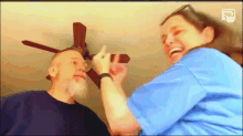a woman in a blue shirt is laughing with a man in a black shirt and a ceiling fan in the background