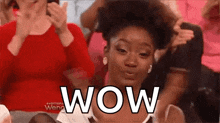 a woman is sitting in a crowd of people and making a surprised face with the word wow .