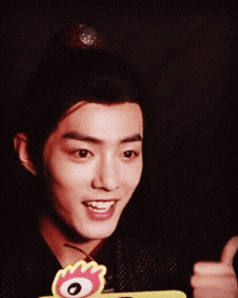 a young man giving a thumbs up in front of a sign that says ' qq ' on it