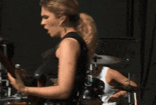 a woman playing a guitar with a drummer behind her
