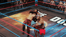 two men are wrestling in a ring with a crowd watching and a sign that says the dojo