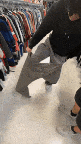 a man is trying on a pair of grey pants in a clothing store