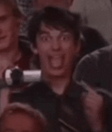 a close up of a man making a funny face in a crowd of people .