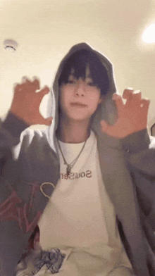 a young man wearing a hoodie and a white shirt is making a funny face with his hands .