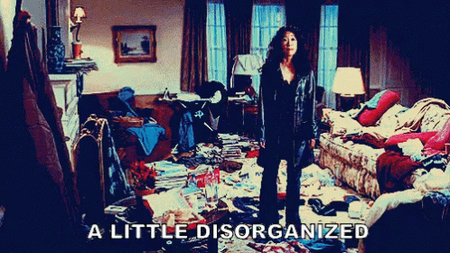 Asian woman with long hair in the midst of a messy room. She spreads her arms and says "a little disorganized"