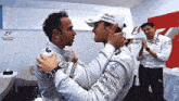 two racing drivers are hugging each other in a locker room .