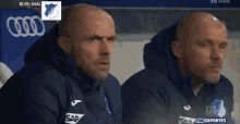 two men wearing sap jackets are watching a game