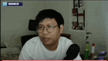 a man wearing glasses and a white shirt is sitting in front of a microphone and a screen that says nbagaming