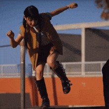 a girl in a brown vest and black shorts is standing on a railing
