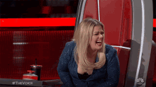 a woman is laughing while sitting in a chair with #thevoice on it