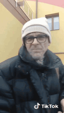a man wearing glasses and a beanie has tiktok written on the bottom of his jacket
