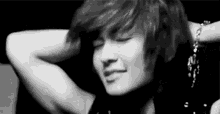a black and white photo of a young man with his eyes closed and his arms behind his head .
